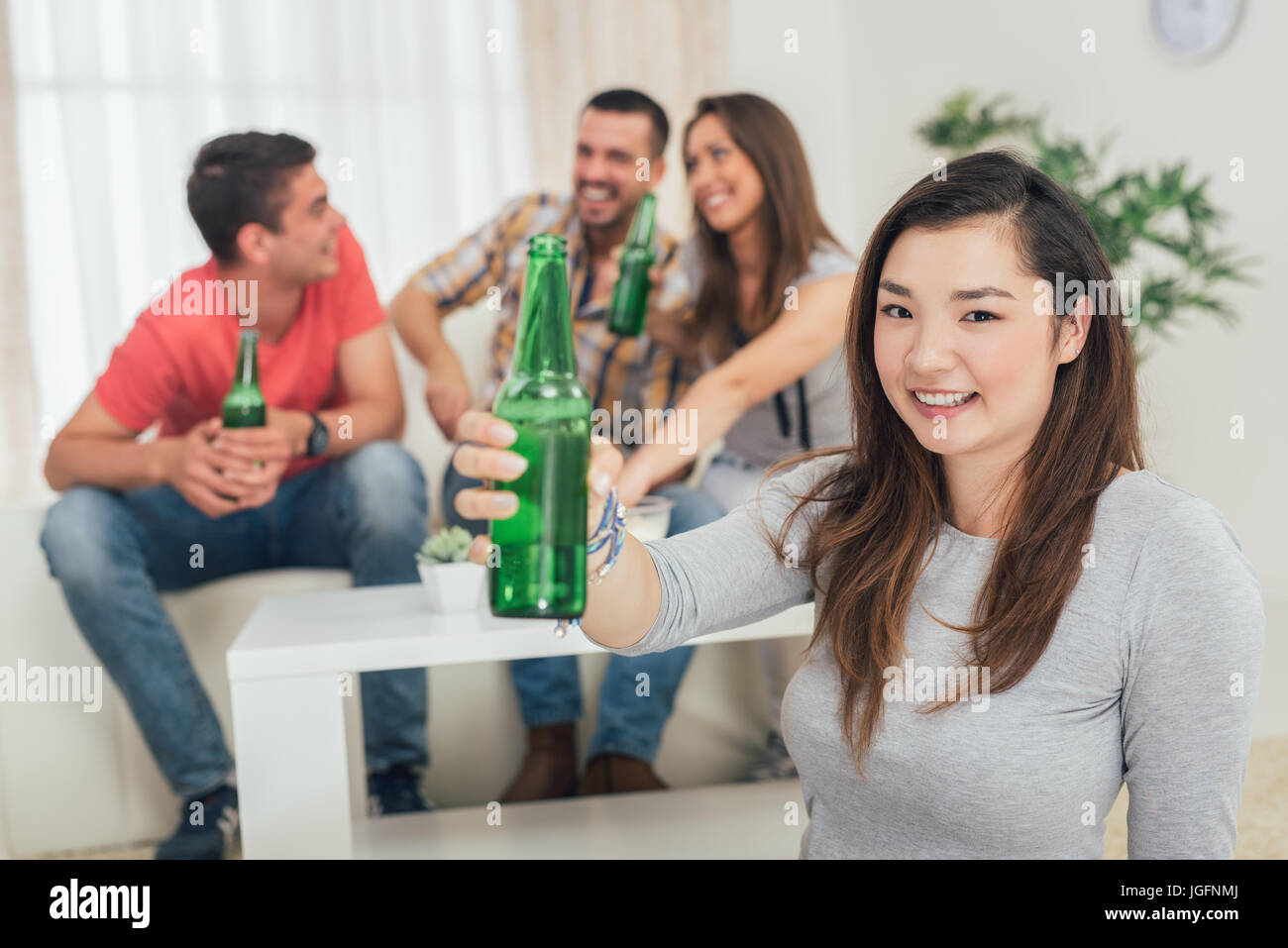 Close up of a young Japanese girl smiling at home party with beer and cheers. Her friends in the background. Selectiv focus. Focus on foreground. Stock Photo