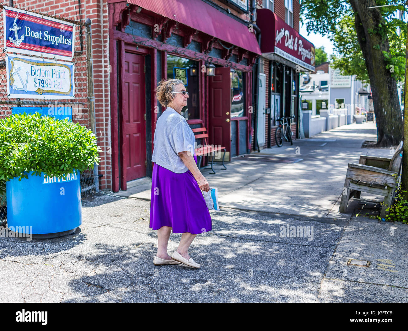 Bronx, USA - June 11, 2017: Older woman walking on sidewalk in outside street in City Island during summer Stock Photo
