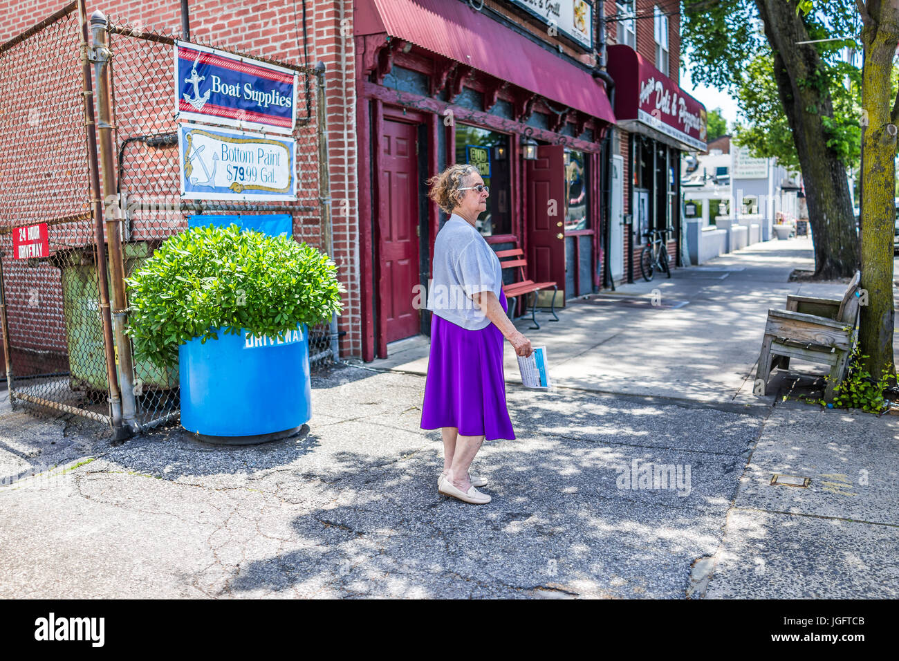 Bronx, USA - June 11, 2017: Older woman walking on sidewalk in outside street in City Island during summer Stock Photo