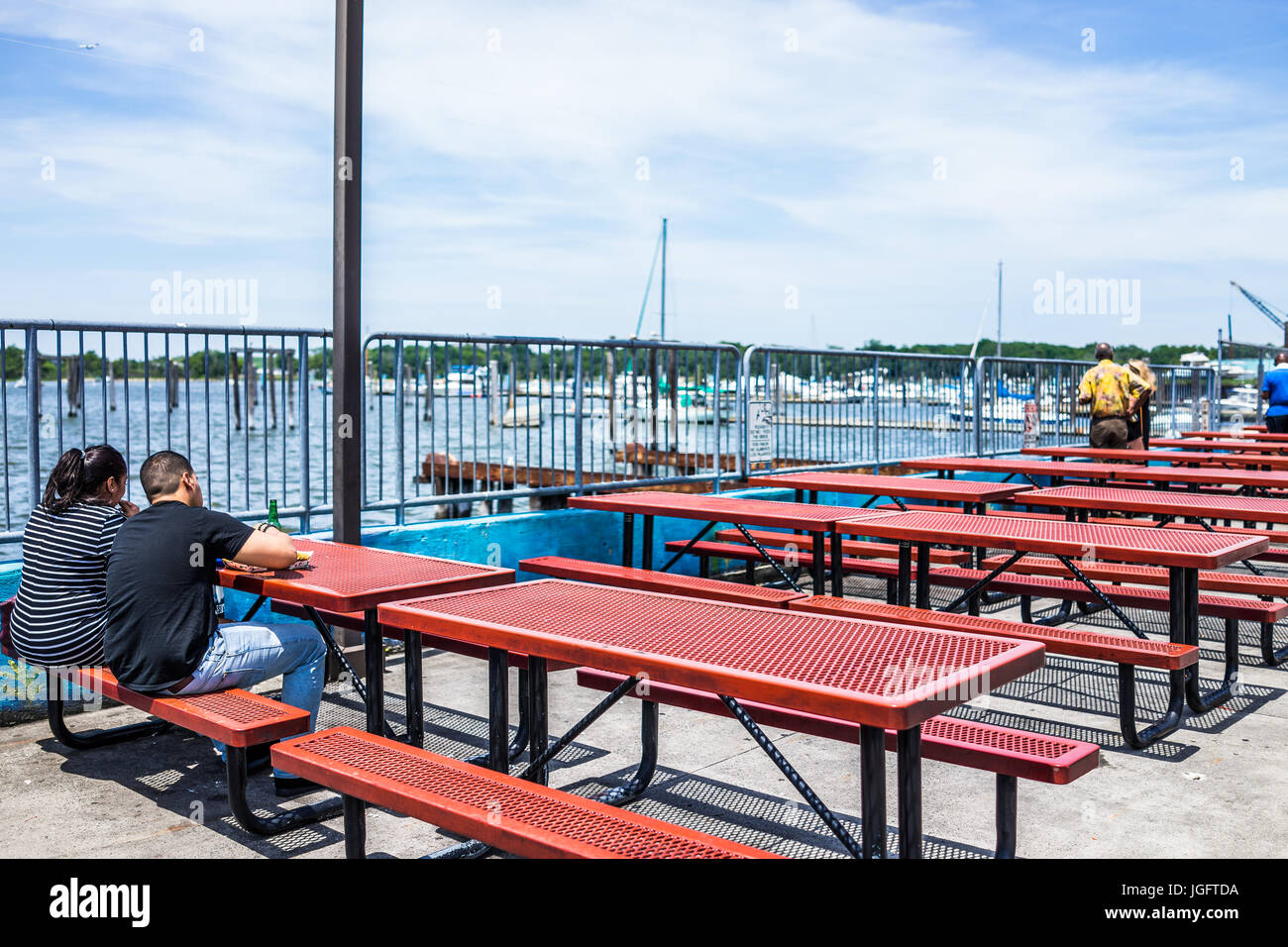 Bronx, USA - June 11, 2017: City Island harbor with boats and people eating lunch on picnic tables by restaurant Stock Photo