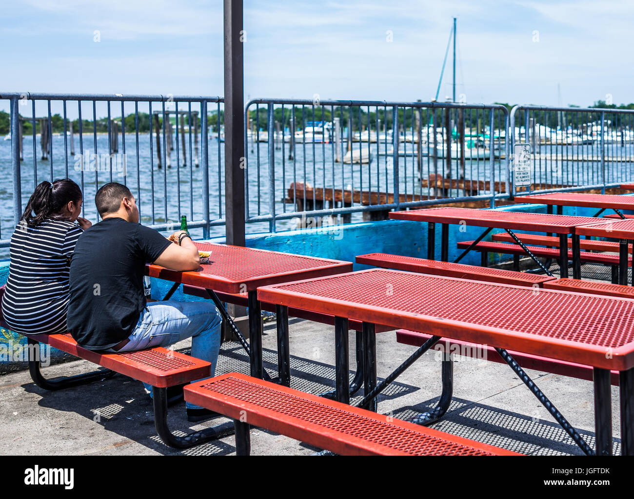 Bronx, USA - June 11, 2017: City Island harbor with boats and people eating lunch on picnic tables by restaurant Stock Photo