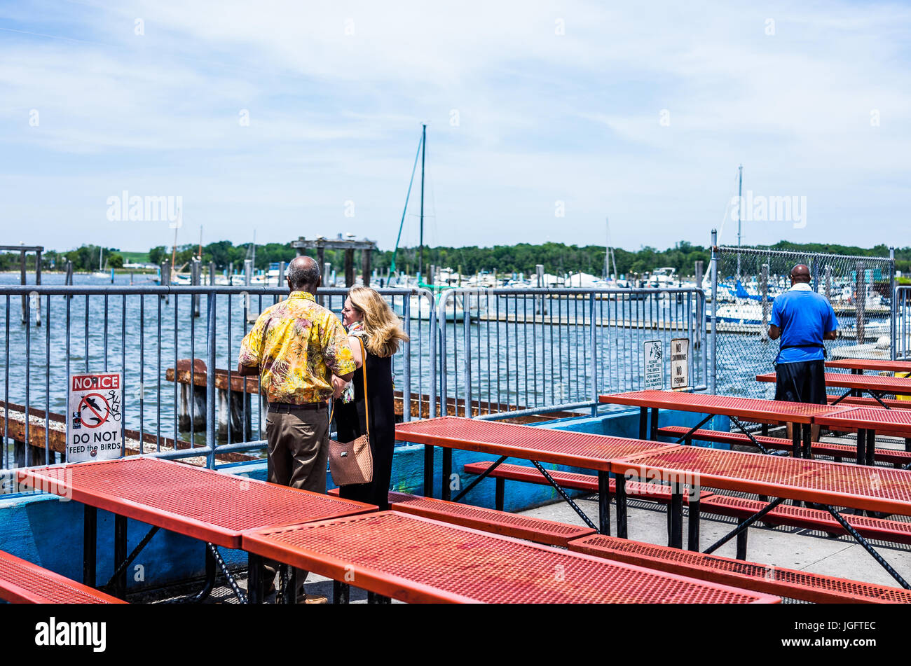 Bronx, USA - June 11, 2017: City Island harbor with boats and people looking at view by picnic tables by restaurant Stock Photo