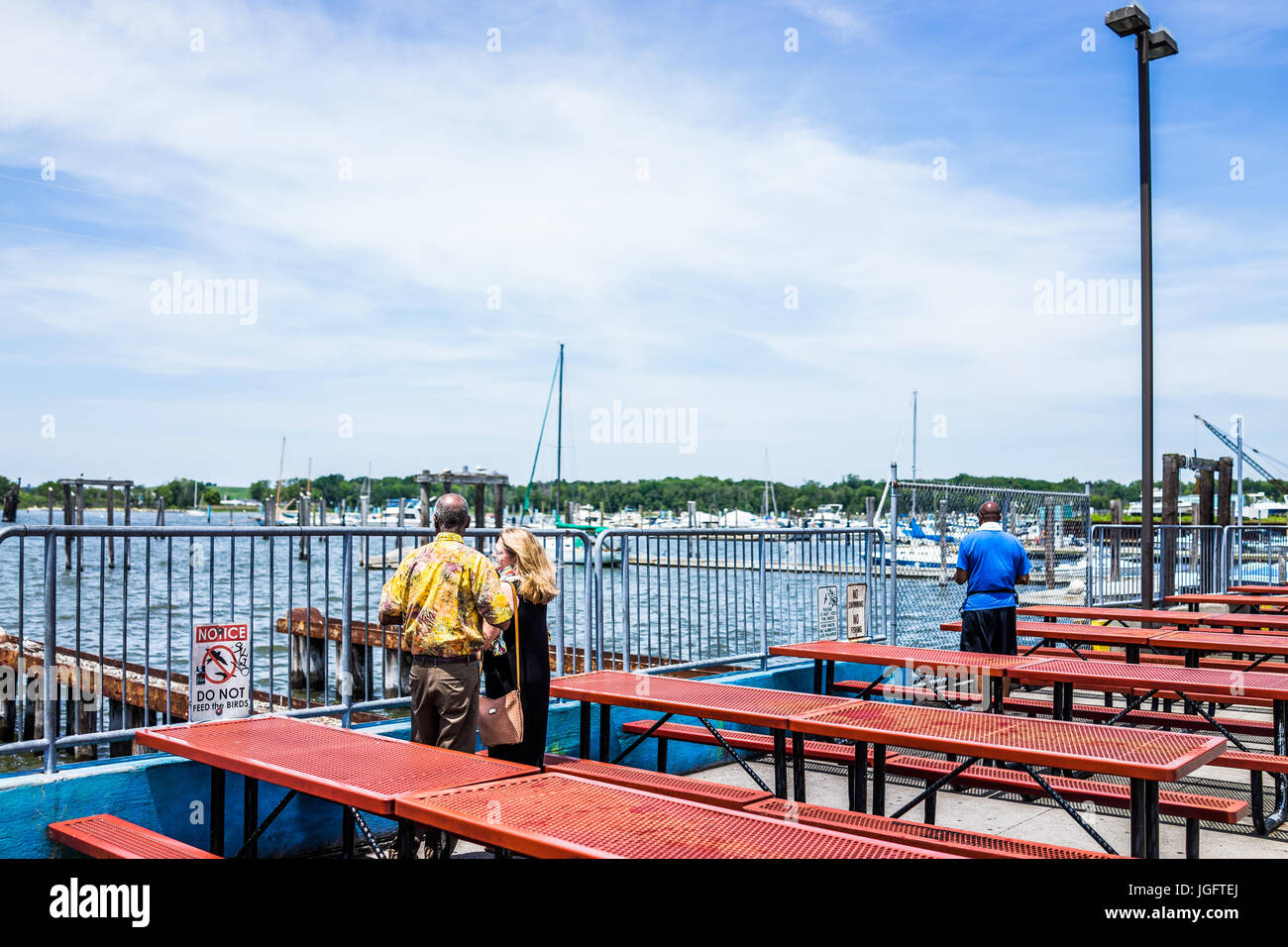 Bronx, USA - June 11, 2017: City Island harbor with boats and people looking at view by picnic tables by restaurant Stock Photo