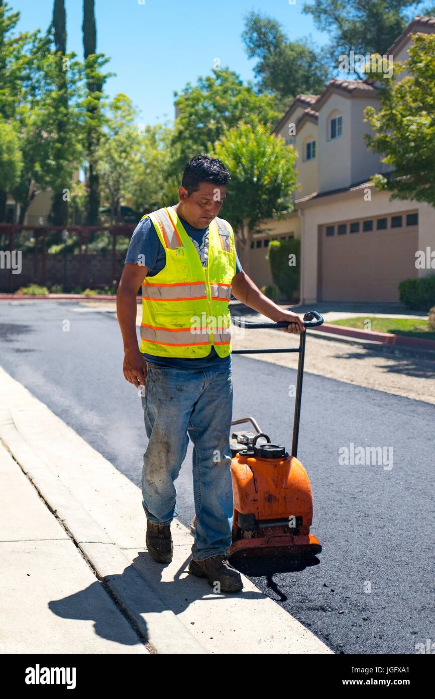 An employee of American Asphalt pulls a manual compactor across a newly laid road surface during a road construction and resurfacing project in the San Francisco Bay Area suburb of San Ramon, California, June 26, 2017. Stock Photo