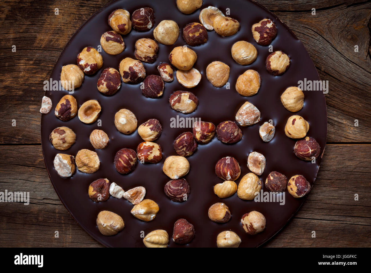 Round artisanal dark chocolate bar with whole hazelnuts on rustic wood background, overhead view Stock Photo