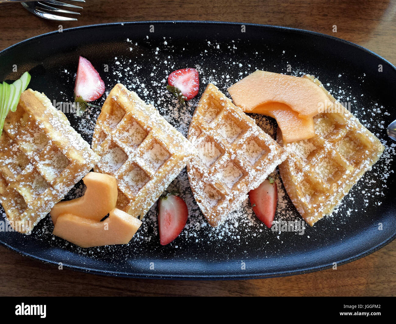 Belgium waffles with fruit and powdered sugar on breakfast plate
