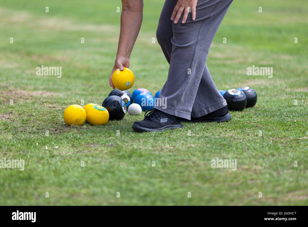 person picking up Grass bowls target practise bright yellow blue grass amateur game legs copy space Stock Photo