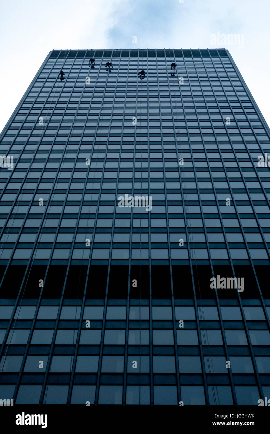 Window cleaners cleaning windows of modern office tower high rise building skyscraper using ropes and bosun's chair Stock Photo