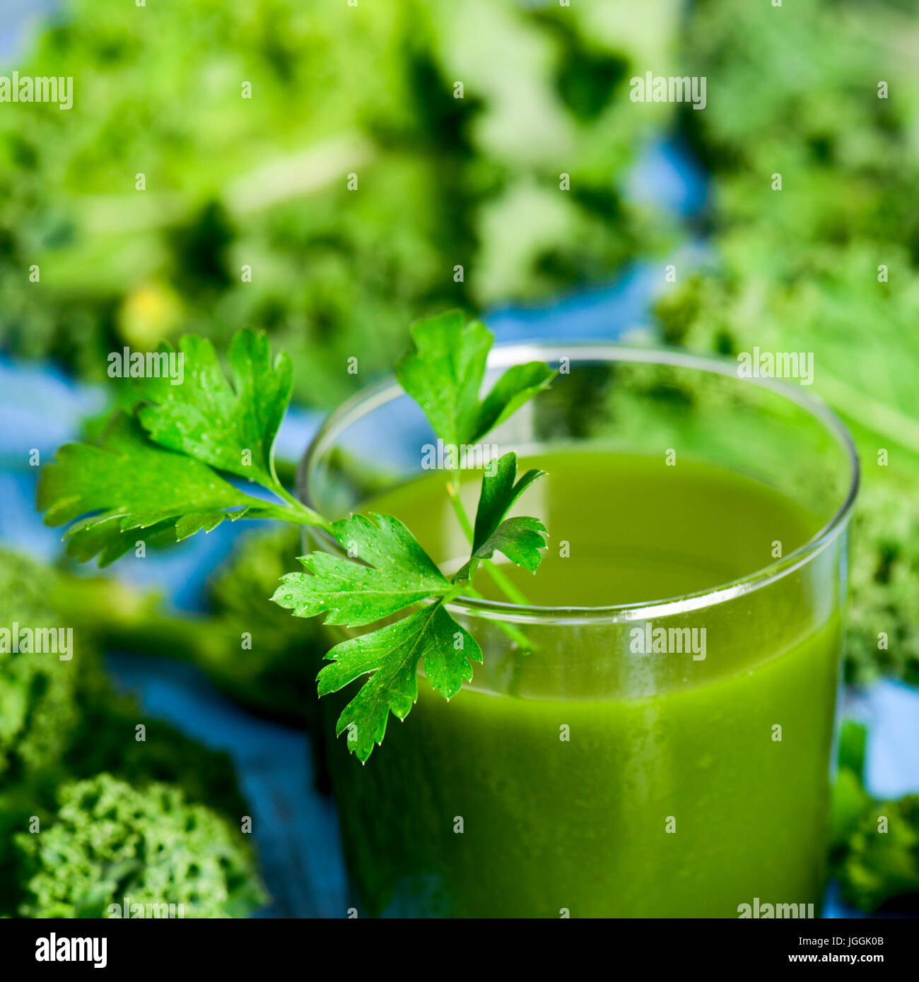 a green smoothie served in a glass topped with a twig of parsley and surrounded by kale leaves kale, on a blue rustic wooden table Stock Photo