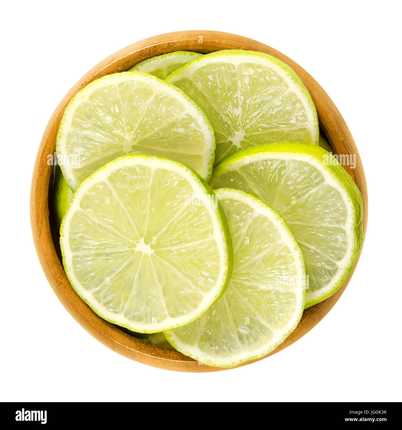 Lime slices in wooden bowl. Fresh cut unripe green edible citrus fruit discs. Key lime, Citrus aurantiifolia. Isolated macro food photo close up. Stock Photo