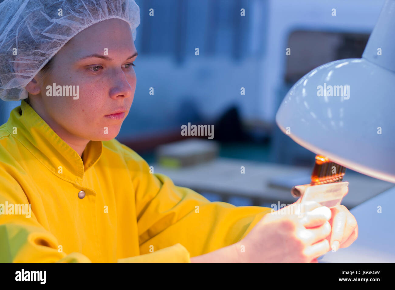 Laboratory technician inspects vials and ampoules for particulates in liquid and container defects. Special light conditions in the lab. Stock Photo