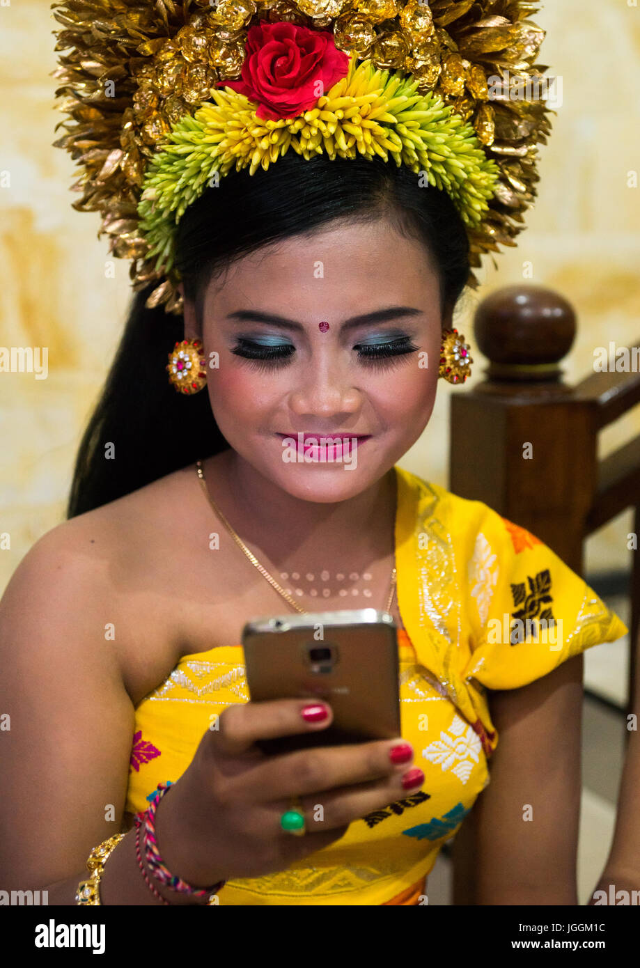 A teenage girl in traditional costume using her mobile phone as a mirror before a tooth filing ceremony, Bali island, Canggu, Indonesia Stock Photo