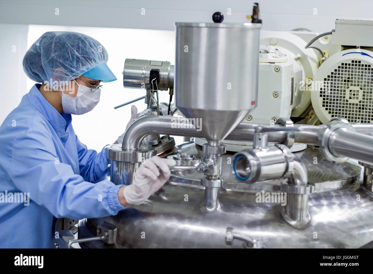 Pharmaceutical technician works in sterile working conditions at pharmaceutical factory. Female worker wearing protective clothing. Stock Photo
