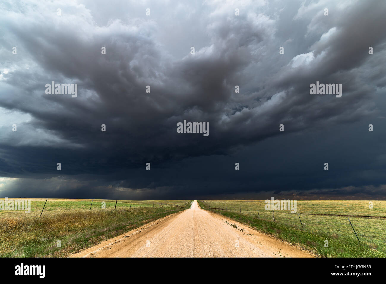 Dirt road and dark clouds with stormy sky over a field in Colorado Stock Photo