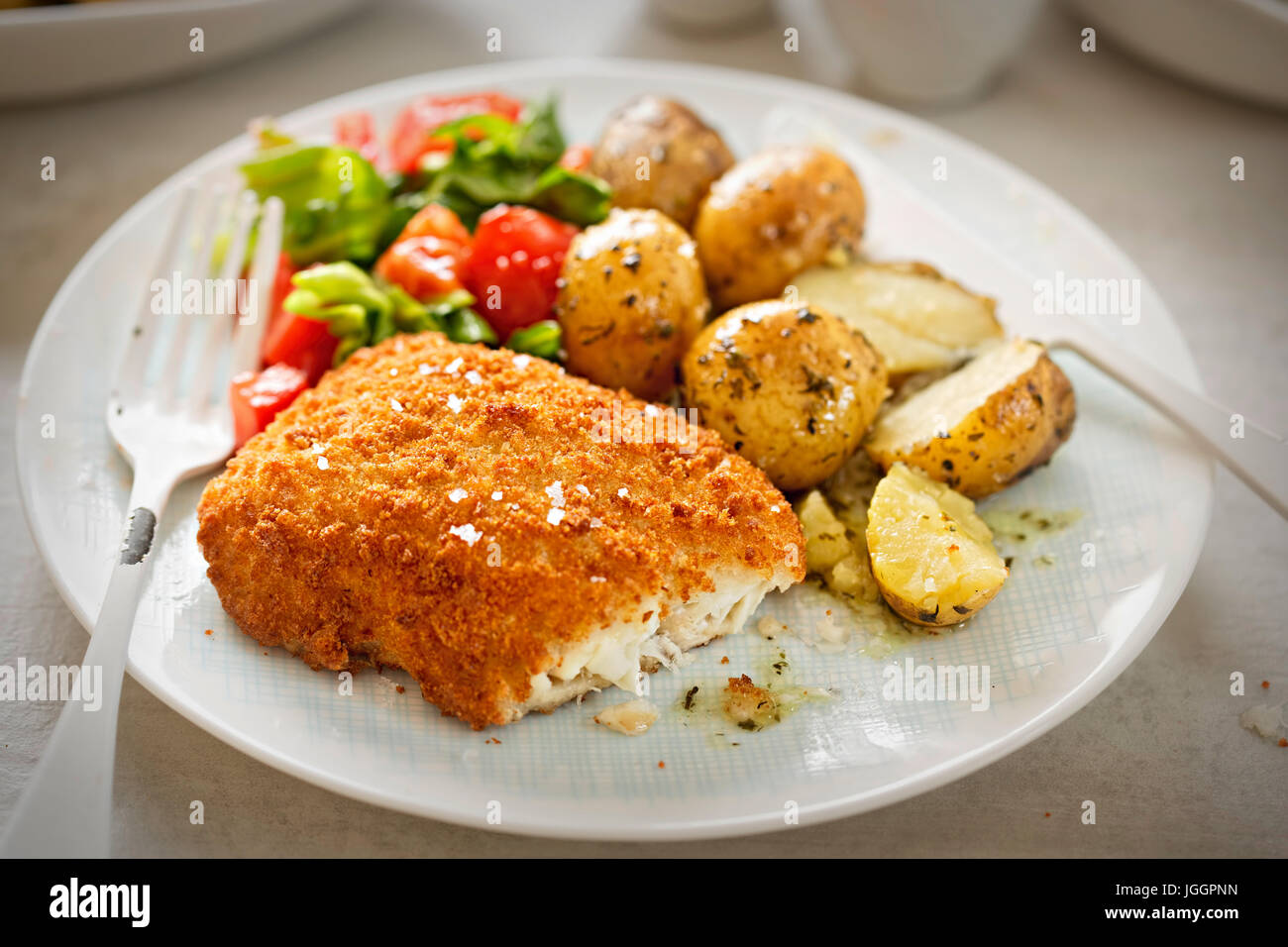 Traditional breaded fillet of cod with baby potatoes and salad Stock Photo