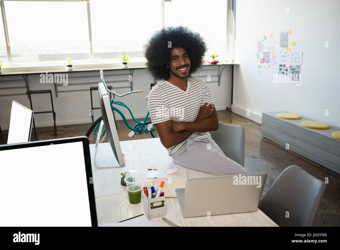 Portrait of smiling young businessman sitting on desk at office Stock ...