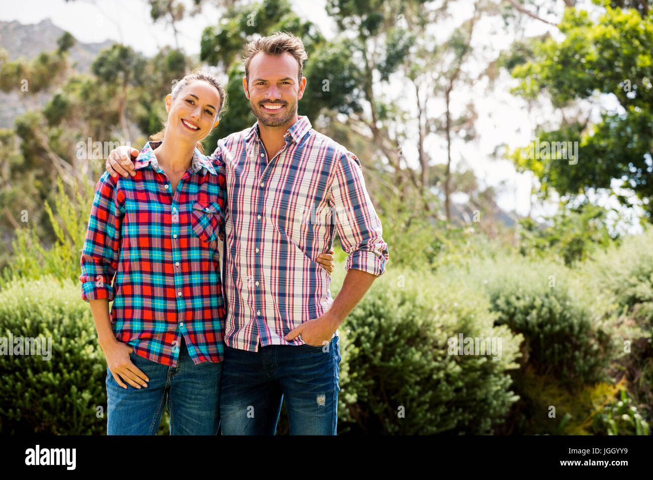 Portrait of smiling couple standing against trees at lawn Stock Photo ...