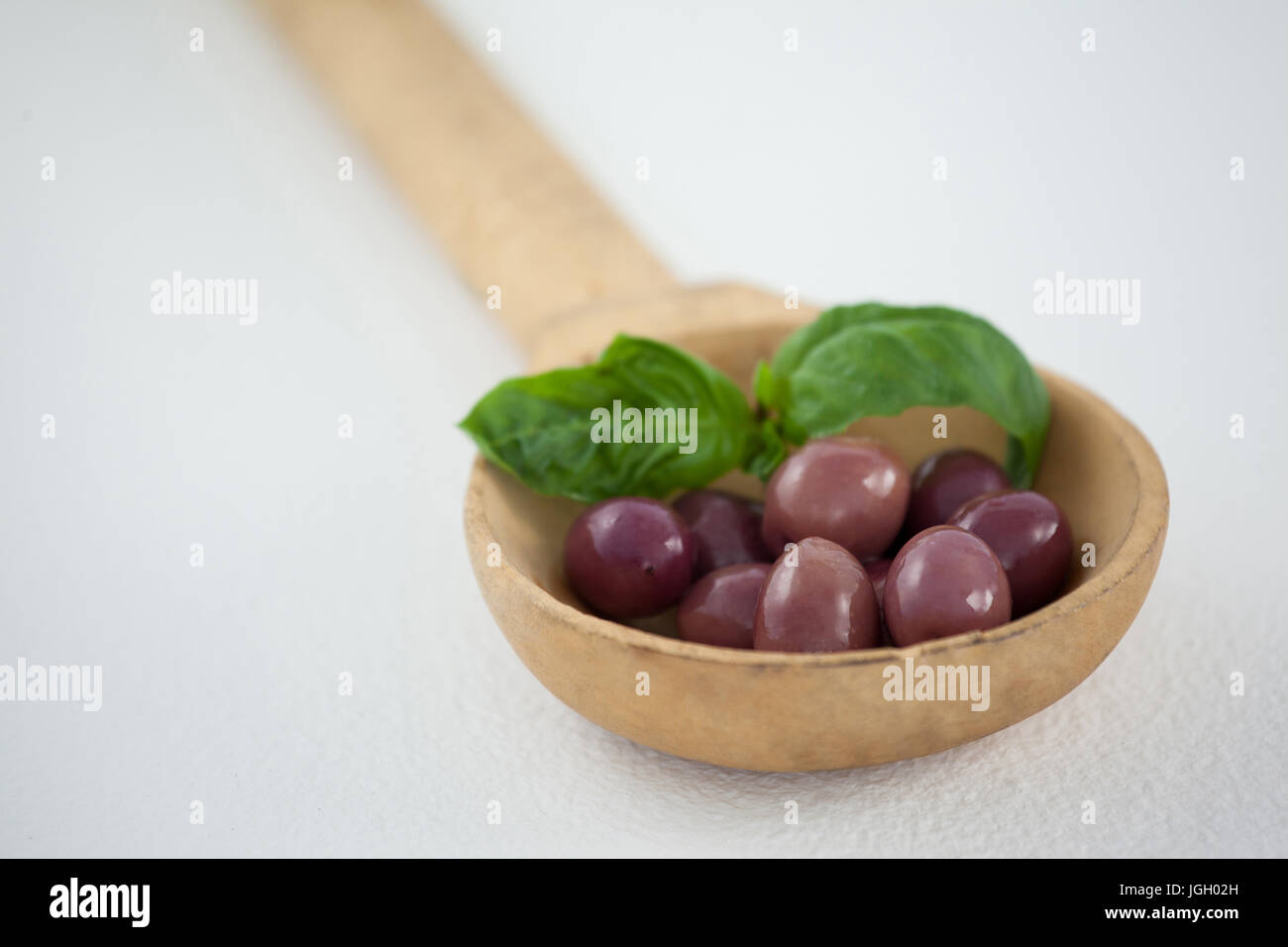Close up of brown olives with herb in woden laddle on ladle Stock Photo