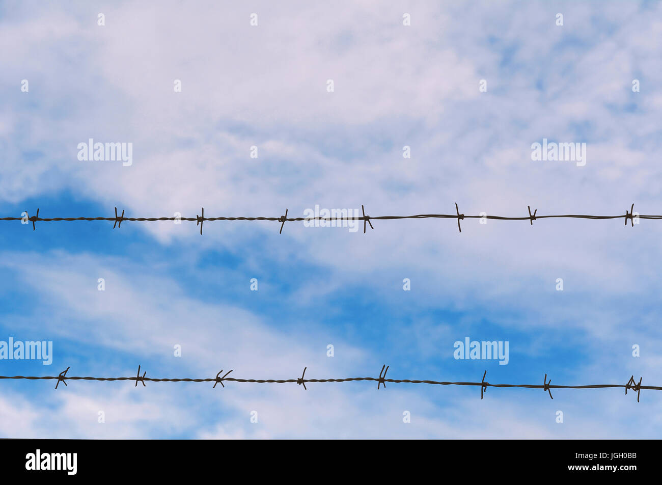 Fence of barbed wire against blue sky with clouds Stock Photo - Alamy