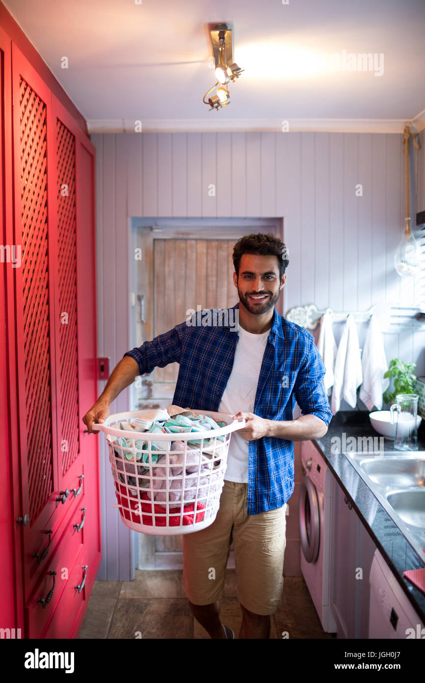 Portrait of man holding laundry basket while standing by sink at home Stock Photo