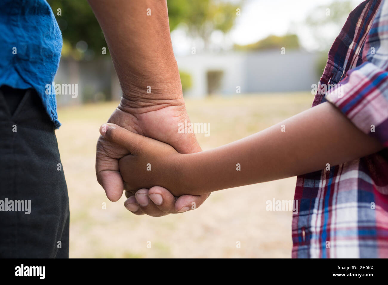 Cropped image of boy and grandfather holding hands while standing in yard Stock Photo