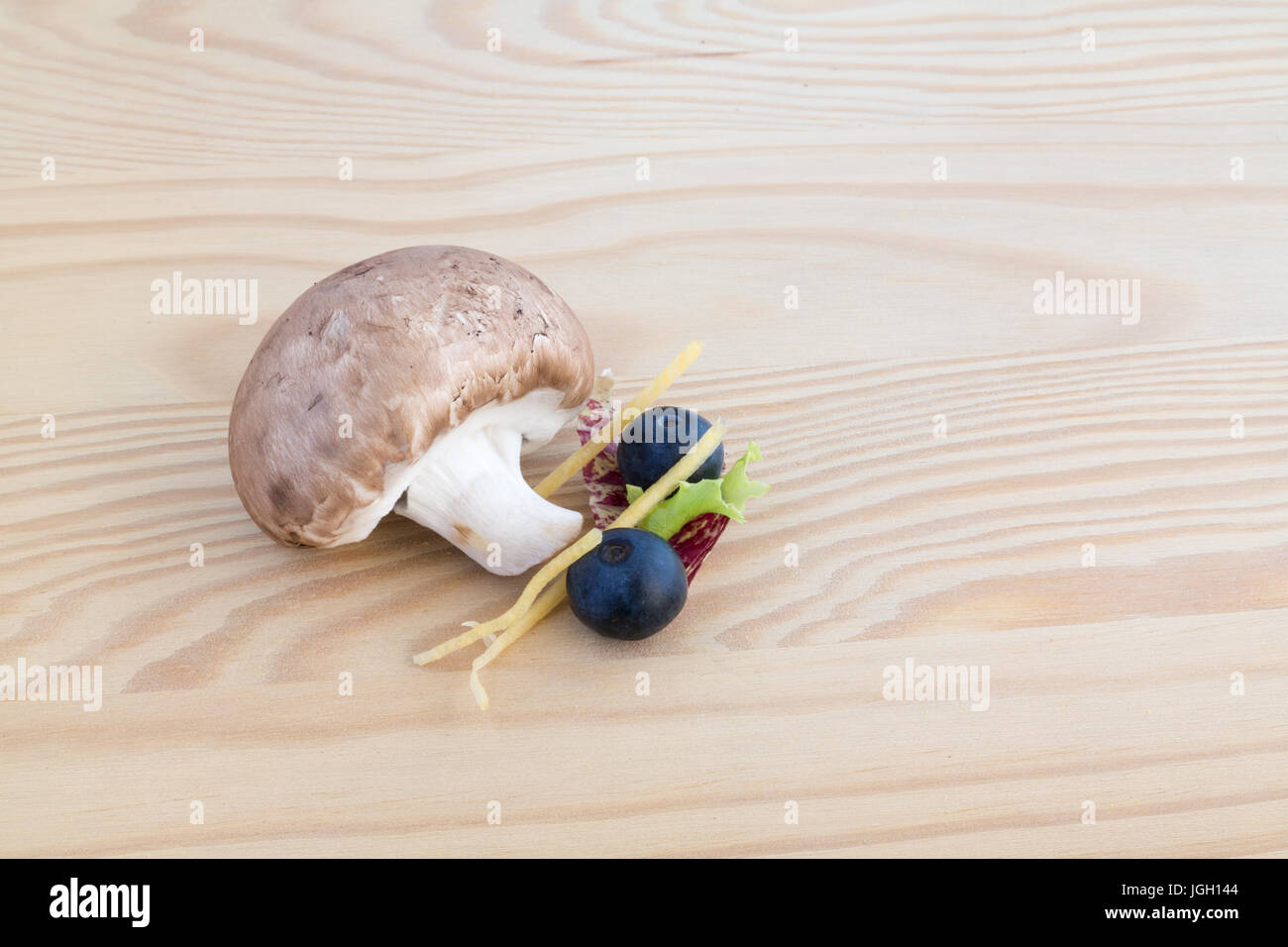 Chestnut mushroom, two blueberries and lettuce leaf on wooden cutting board Stock Photo