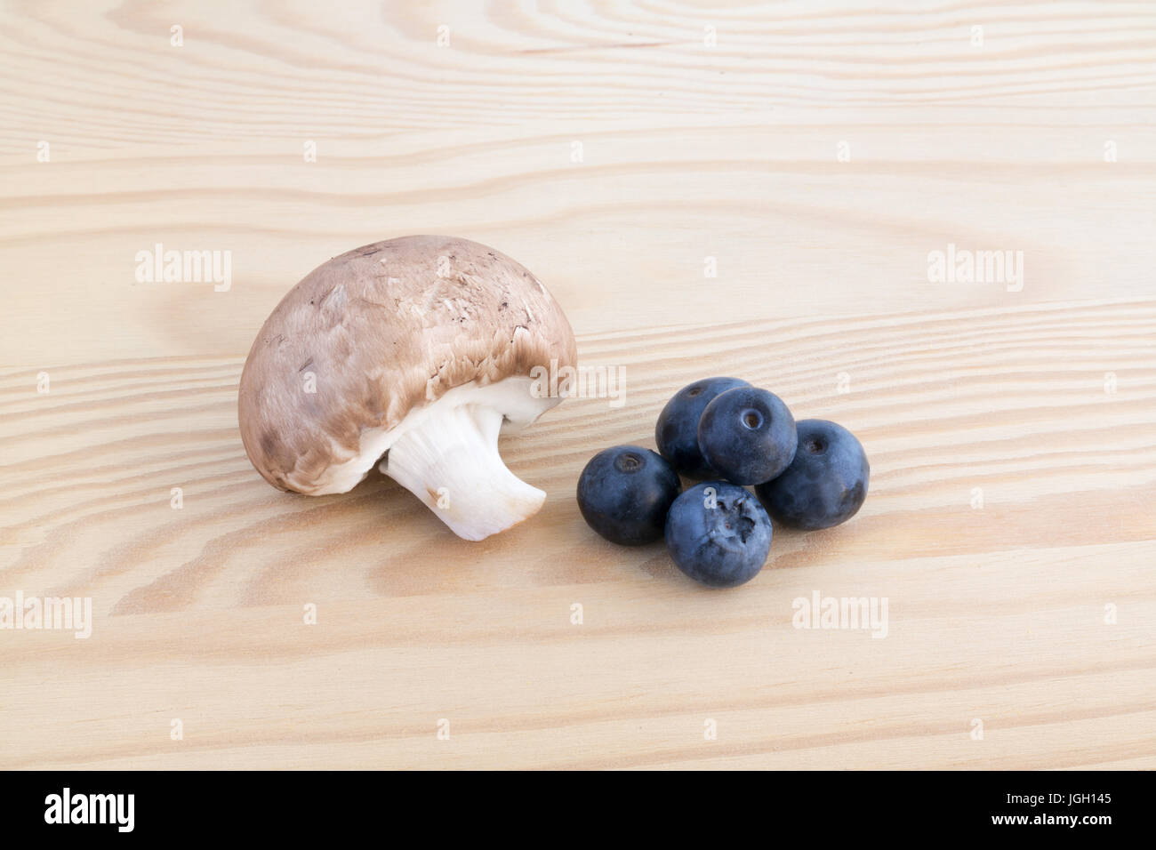 Chestnut mushroom and four blueberries on wooden cutting board Stock Photo