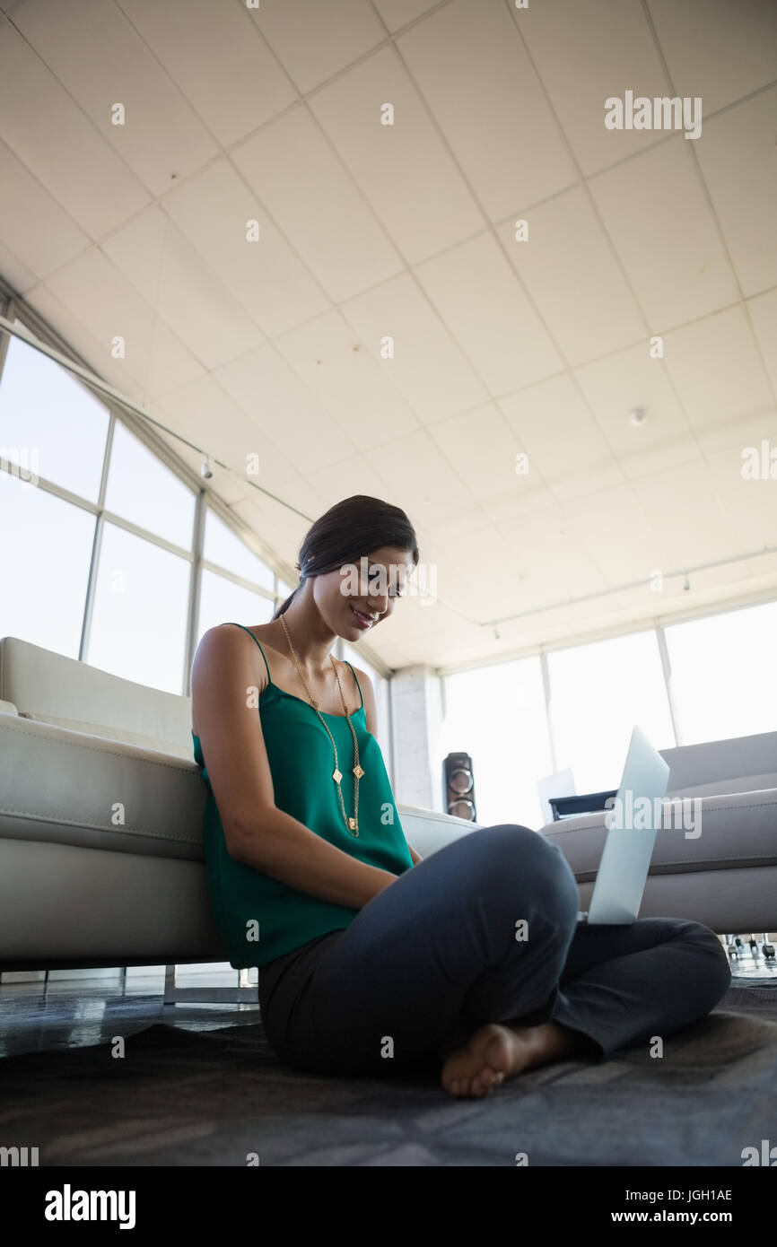 Young woman using laptop while relaxing by sofa at office Stock Photo ...