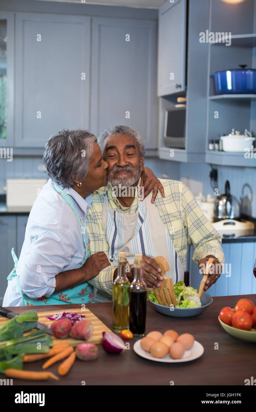 Side view of woman kissing man while preparing food in kitchen at home ...