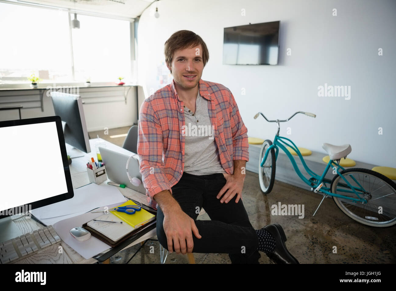 Portrait of young businessman sitting on desk at office Stock Photo - Alamy