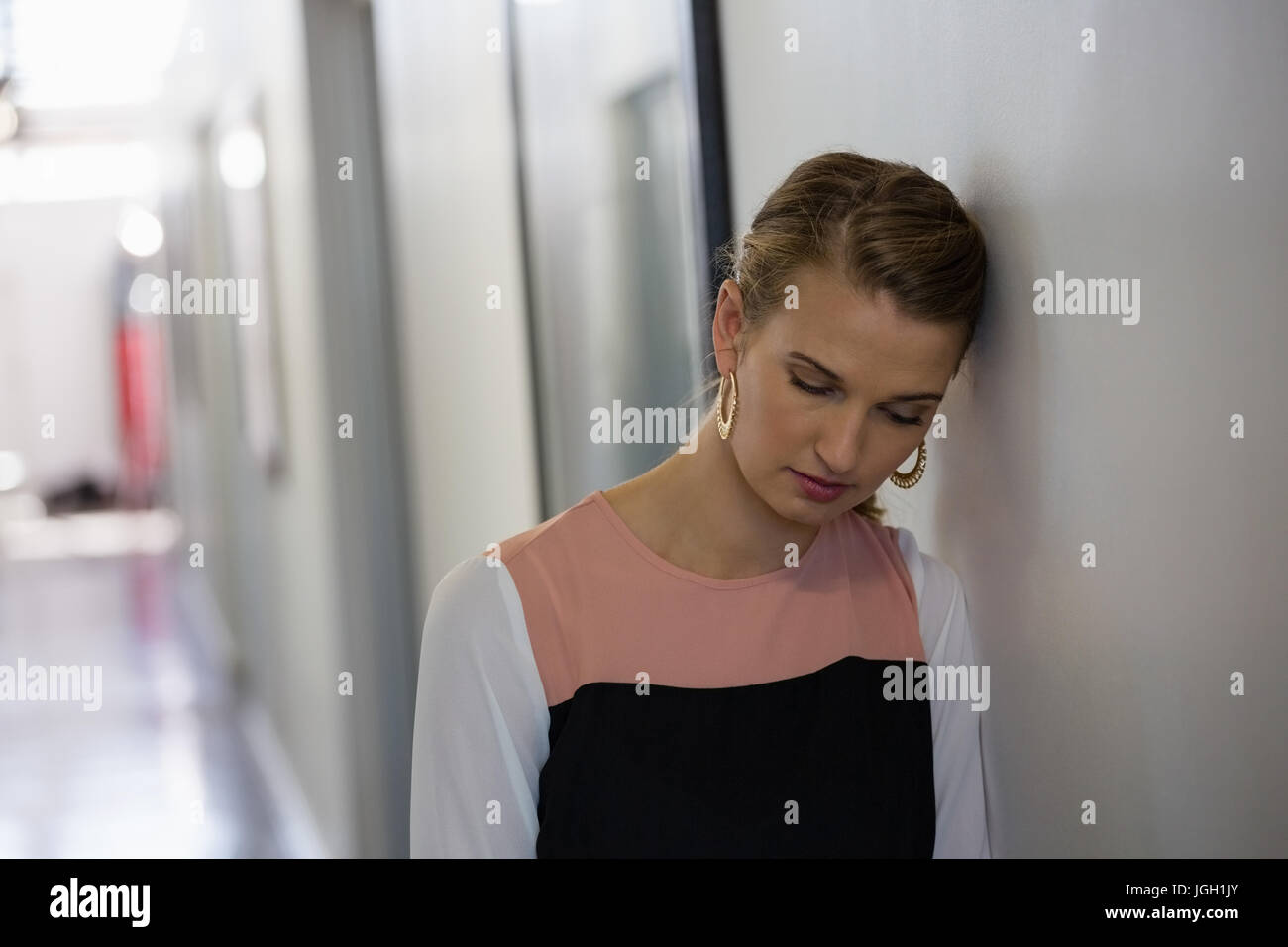 Sad young businesswoman leaning on wall at creative office Stock Photo