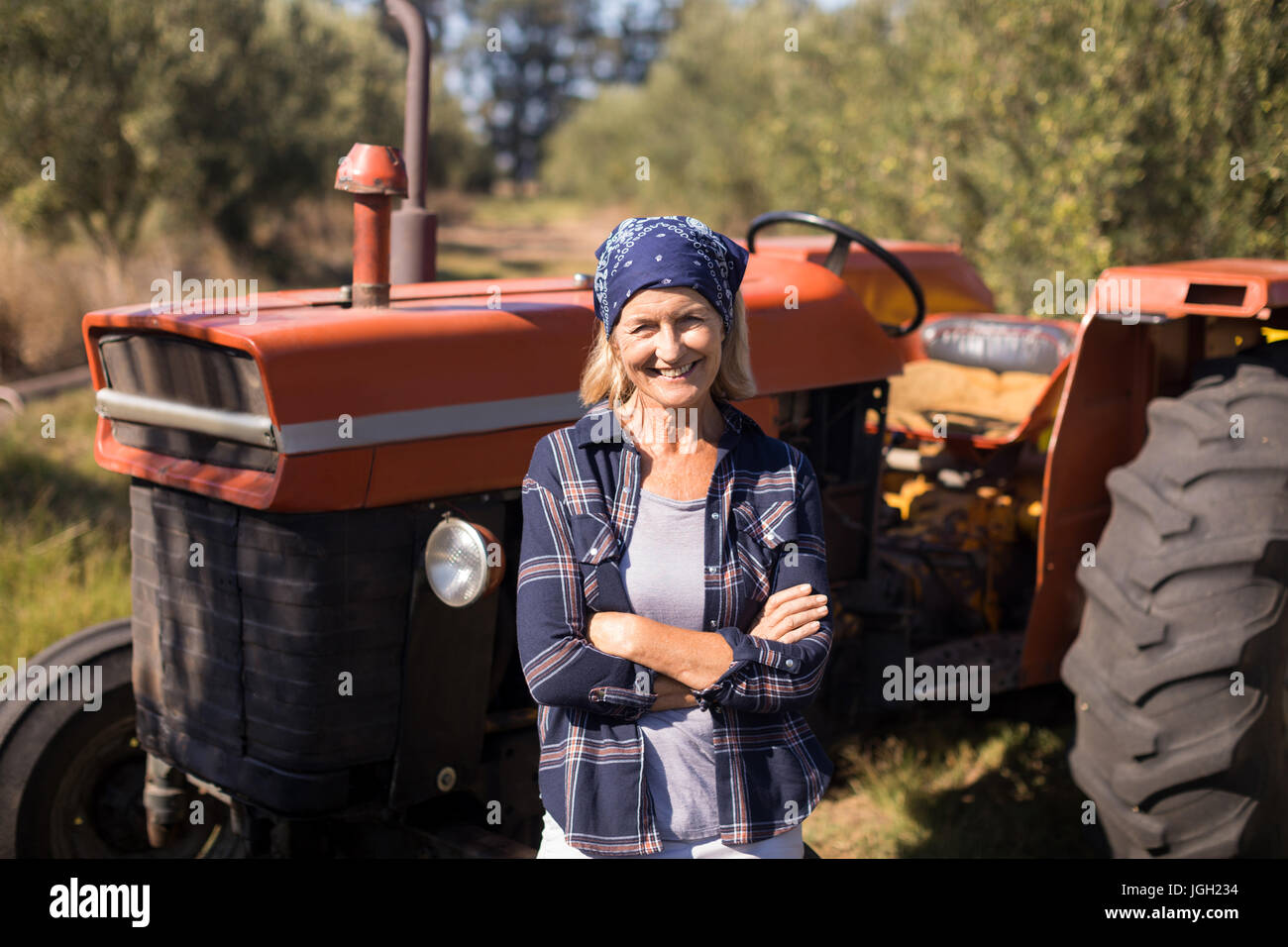 Portrait of happy woman standing with arms crossed against tractor in ...