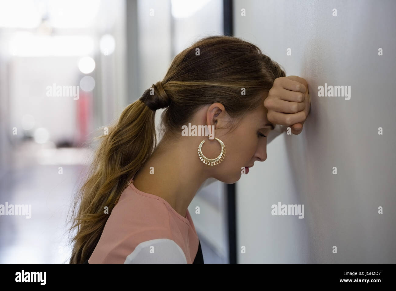 Sad young businesswoman leaning on wall at office Stock Photo