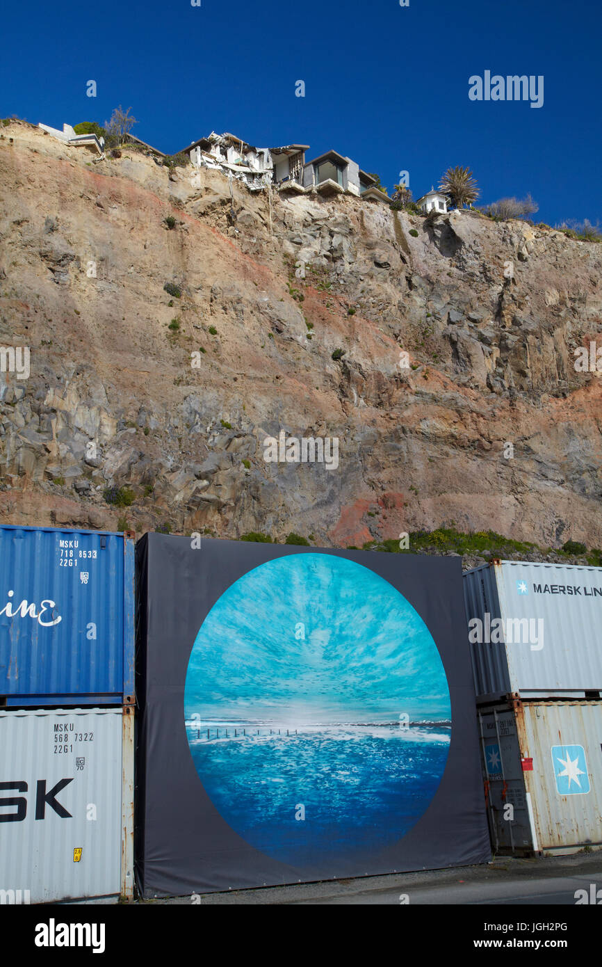 Clifftop house damaged by earthquake, and shipping containers protecting traffic from falling debris, Sumner, Christchurch, Canterbury, South Island,  Stock Photo