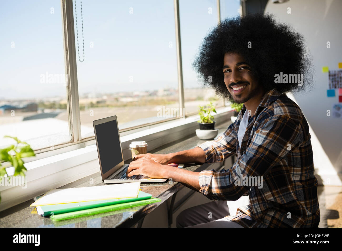 Portrait of smiling young businessman using digital tablet by window at ...