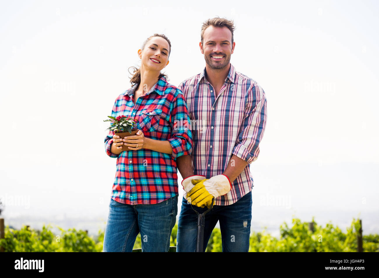 Portrait of smiling woman with man holding potted plant against sky at ...