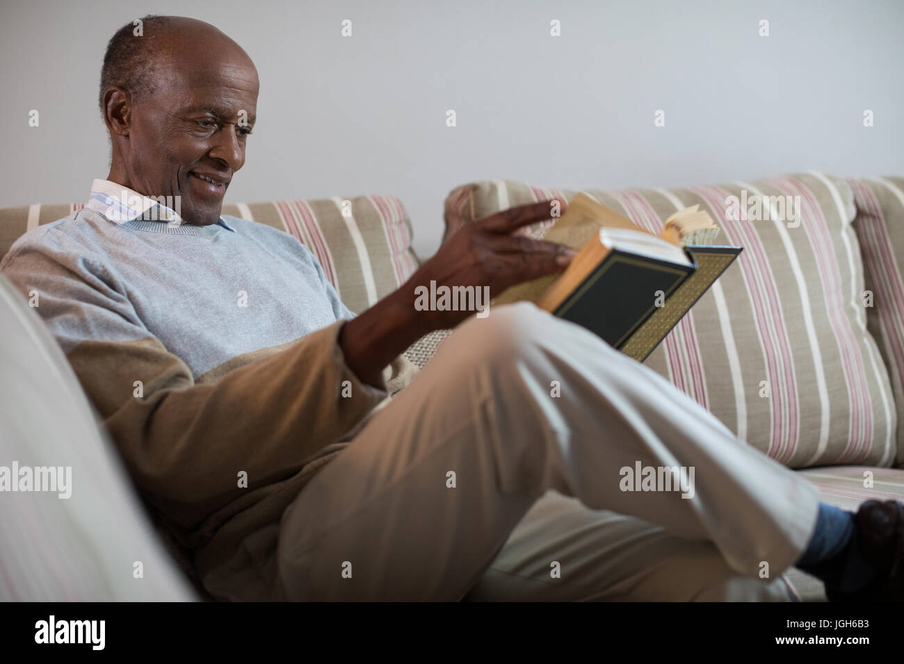 Smiling senior man reading book while sitting on sofa at home Stock Photo