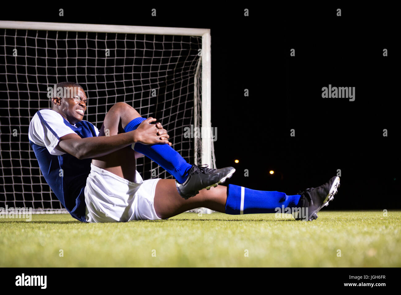 Young male soccer player suffering from knee pain sitting on playing