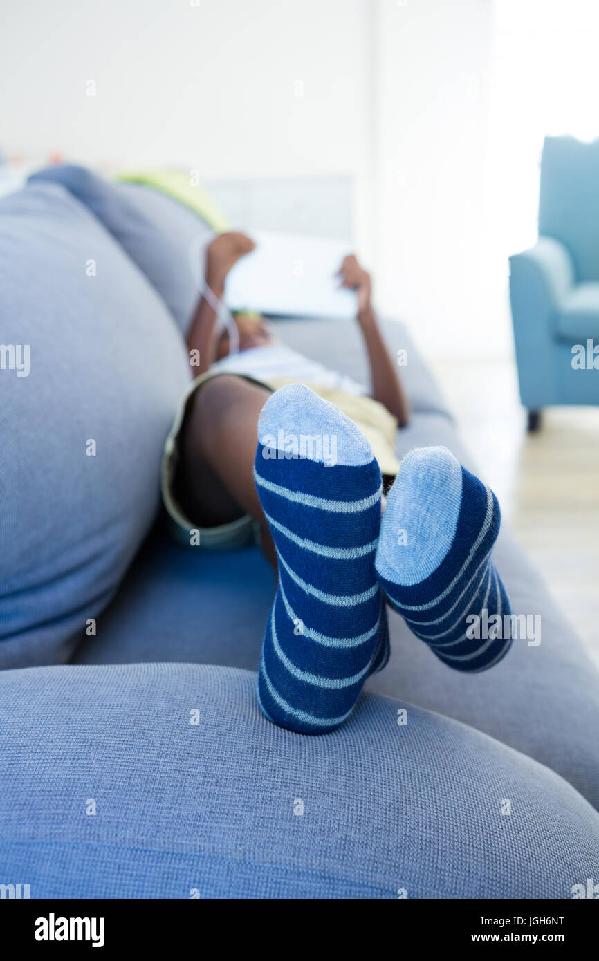 Boy using digital tablet while lying on sofa in living room at home ...