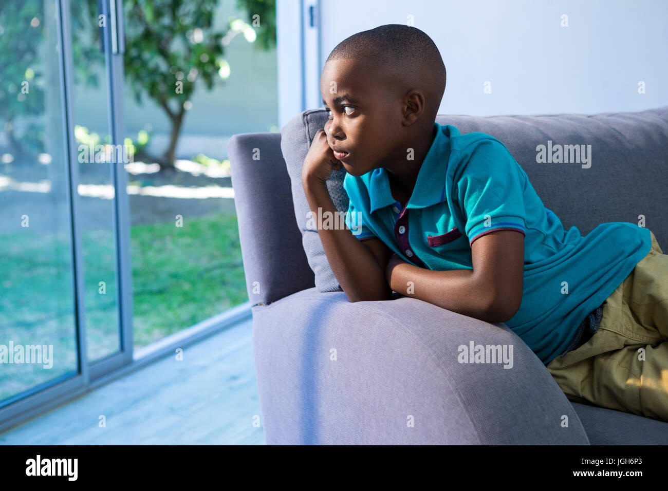 Thoughtful boy looking away while sitting on sofa at home Stock Photo ...