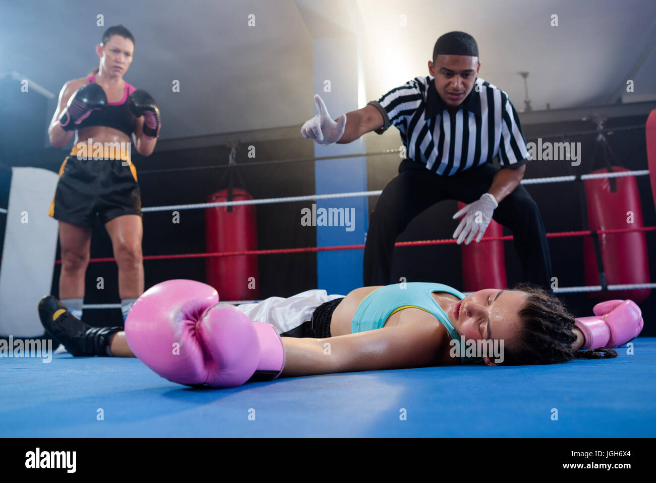 Female boxer looking while referee counting by athlete in boxing ring Stock Photo