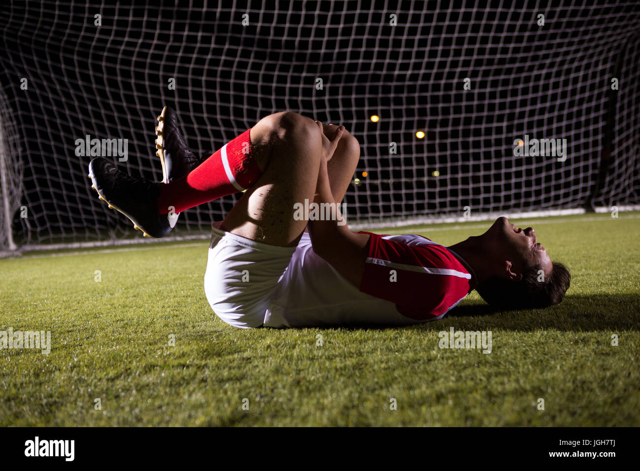 Side view of young male soccer player suffering from knee pain lying down on playing field Stock