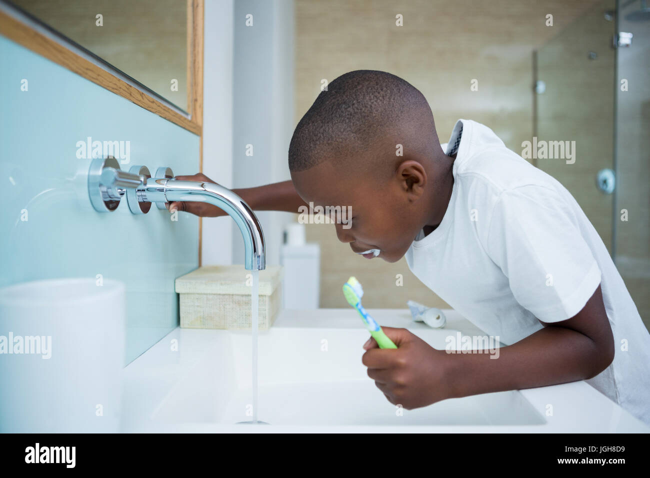 Side view of boy spitting while holding brush in sink at domestic