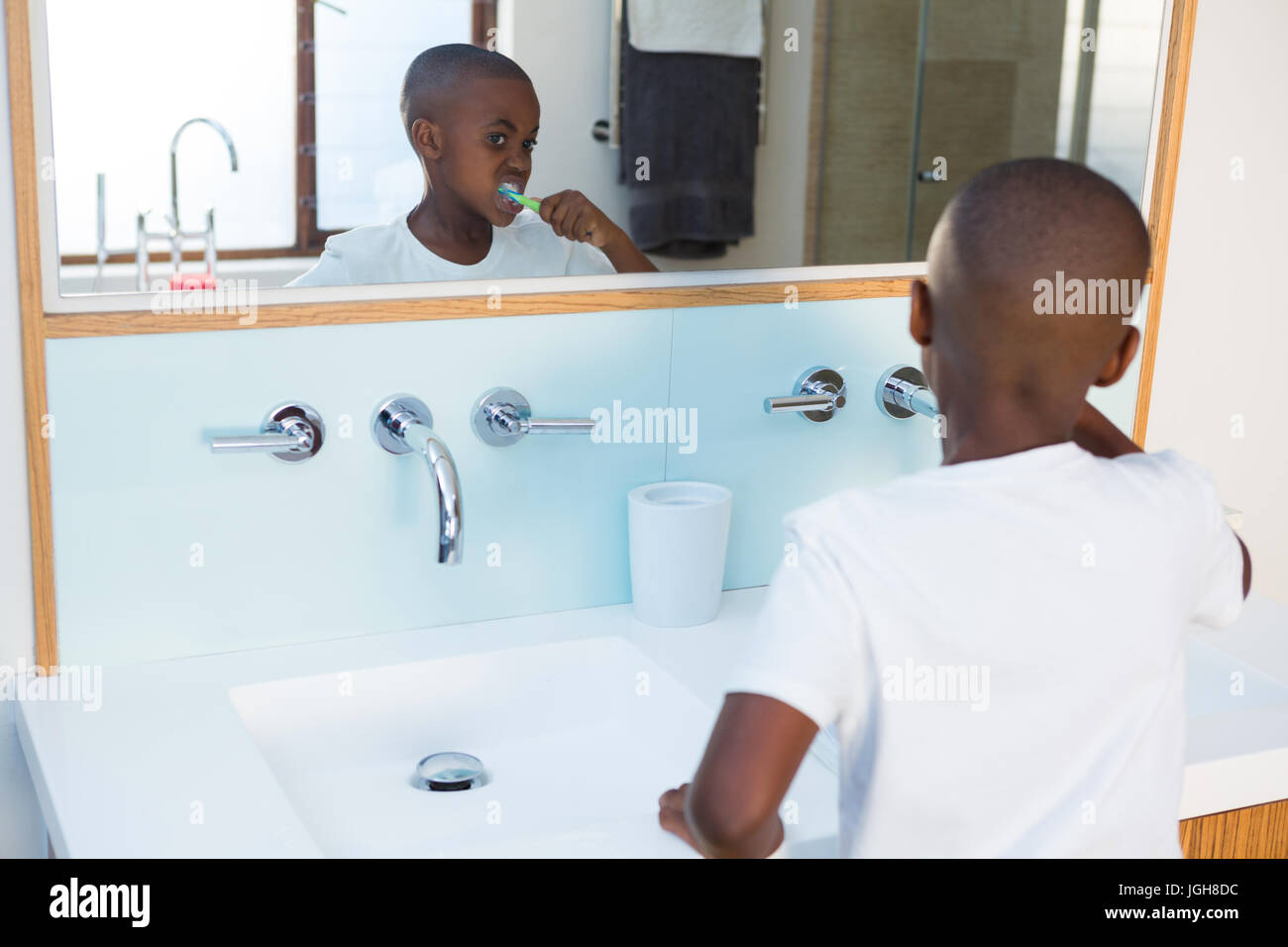 Boy brushing teeth looking at mirror reflection at domestic bathroom