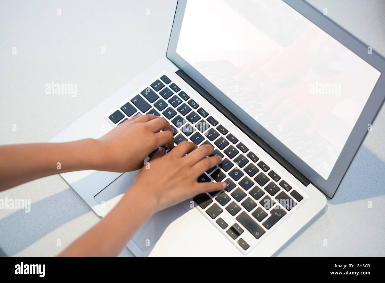 High angle view of girl typing on laptop keyboard at kitchen counter