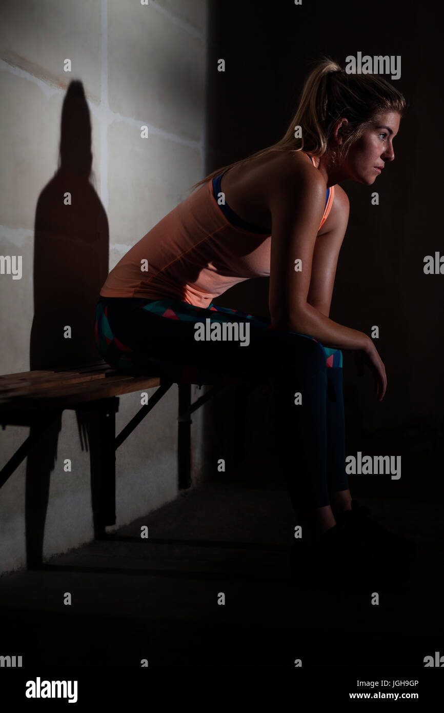 Thoughtful woman relaxing on bench in fitness studio Stock Photo - Alamy