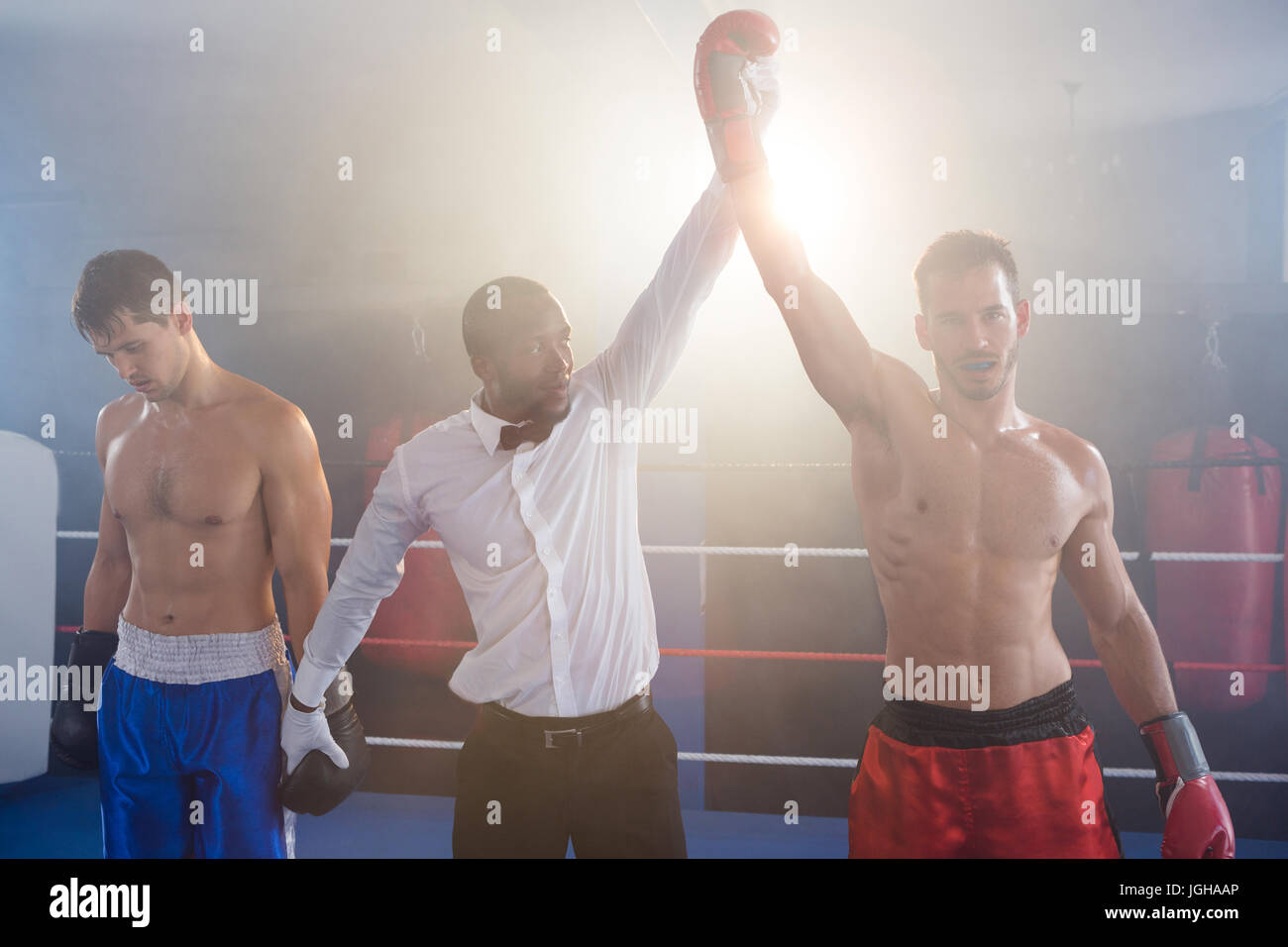 Referee lighting hand of winner standing with loser in boxing ring