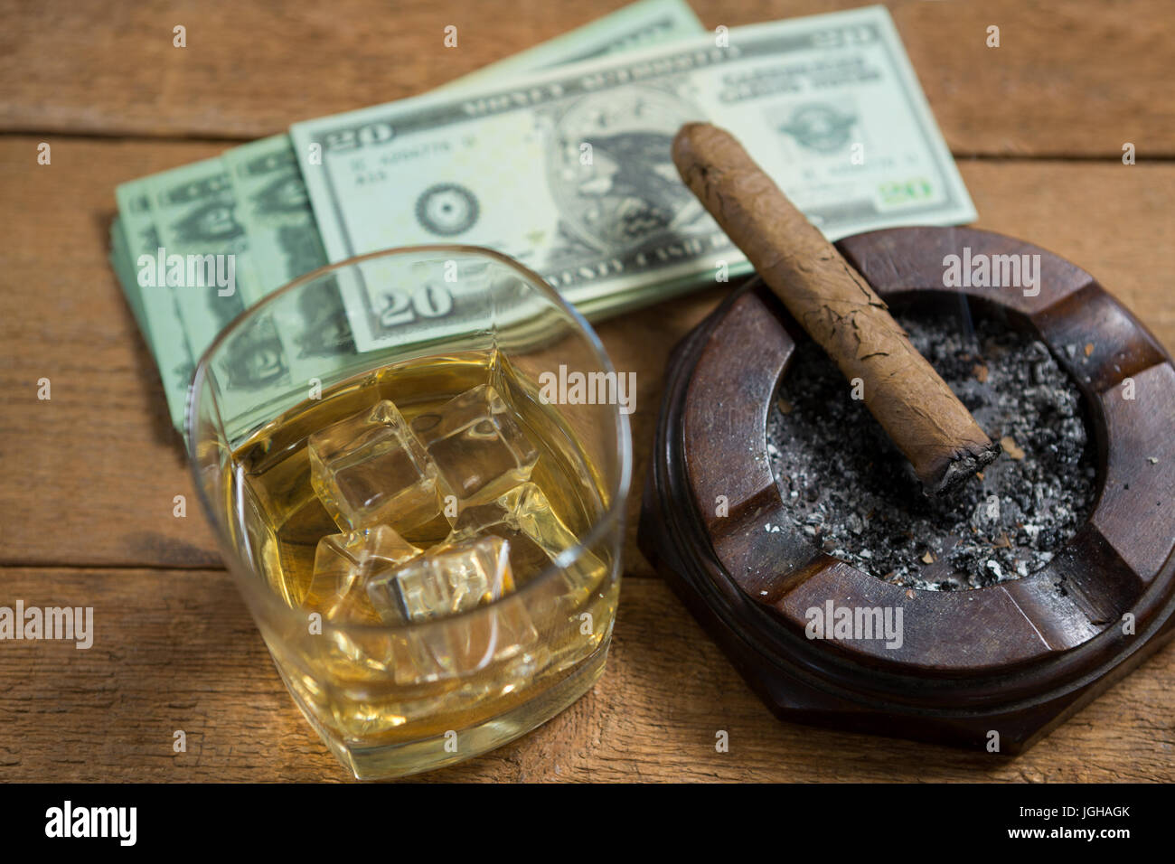 High angle view of whisky and cigar by paper currency on wooden table Stock Photo