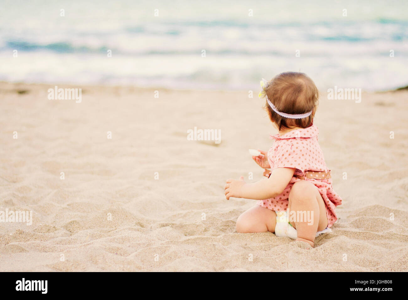 Cute baby girl with a dress on polka dots sitting on the sand on seashore  and looks out to the sea Stock Photo - Alamy