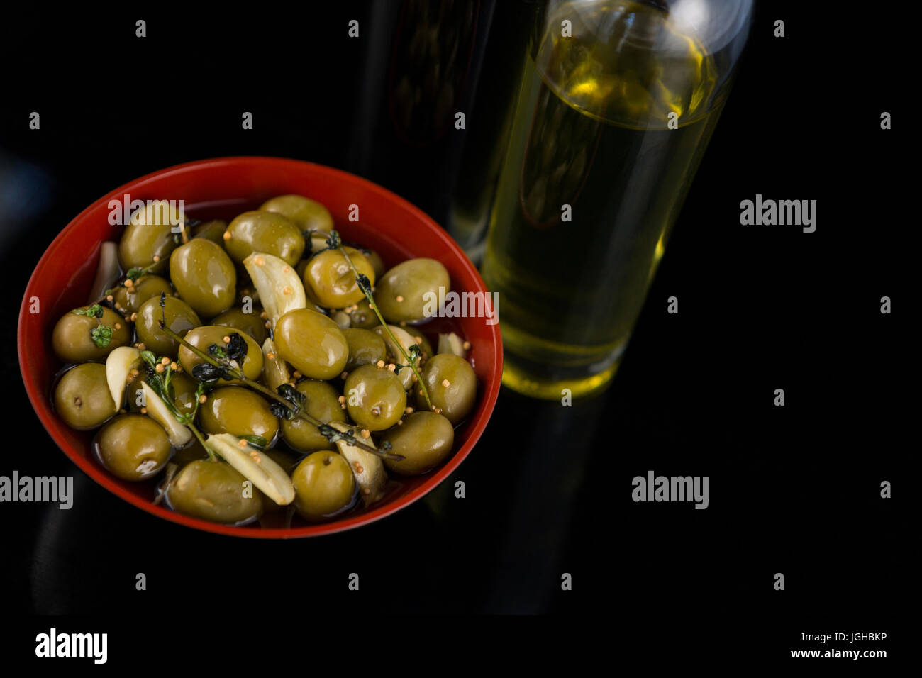 Closeup of marinated olives with olive oil and balsamic vinegar bottle against black background